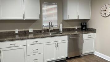 A kitchen with white cabinets, a stainless steel sink, a coffee maker, and a clock on the wall.