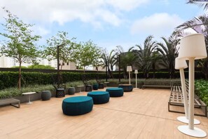 An outdoor seating area with round tables and chairs, surrounded by greenery and palm trees. - Panoramic Skyline Studio in São Paulo (São Paulo)