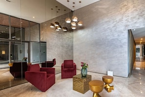 Een moderne lobby met rode stoelen, een gouden vaas en een geometrisch lamp.