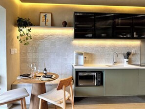 A modern kitchen with a dining area, featuring a built-in microwave, a sink, and a cabinet with glass doors. - Panoramic Skyline Studio in São Paulo (São Paulo)
