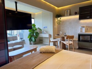 A modern hotel room with a bed, a seating area with a table, a kitchen area, and a large window offering a city view. - Panoramic Skyline Studio in São Paulo (São Paulo)