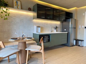 A modern kitchen with a dining area, featuring a built-in microwave, a refrigerator, and a coffee machine. - Panoramic Skyline Studio in São Paulo (São Paulo)