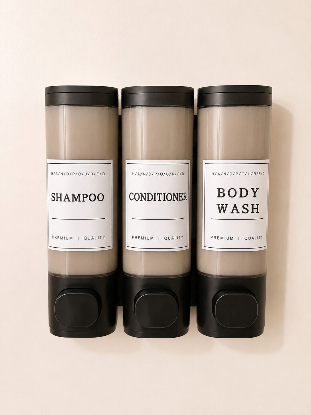 Drei zylindrische Behälter mit den Aufschriften 'SHAMPOO', 'CONDITIONER' und 'BODY WASH', mit schwarzem Boden.