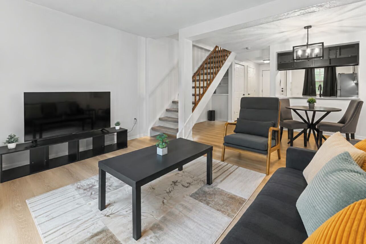 A modern living room with a flat-screen TV, a coffee table, a sofa, and a staircase leading to an upper level.