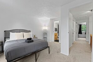 A bedroom with a bed, bedside table, lamp, and a view into another room. - The Gunners Lake Gem: Modern 2BR Furnished Townhouse (Germantown)