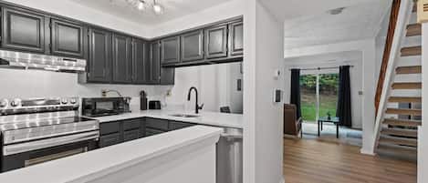 A modern kitchen with dark cabinets, stainless steel appliances, and a white countertop.
