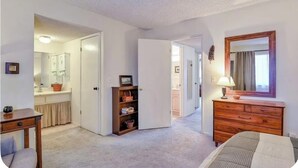 Ein Zimmer mit einem Bett, einem Schminktisch, einem Spiegel und einer Tür zu einem Badezimmer.