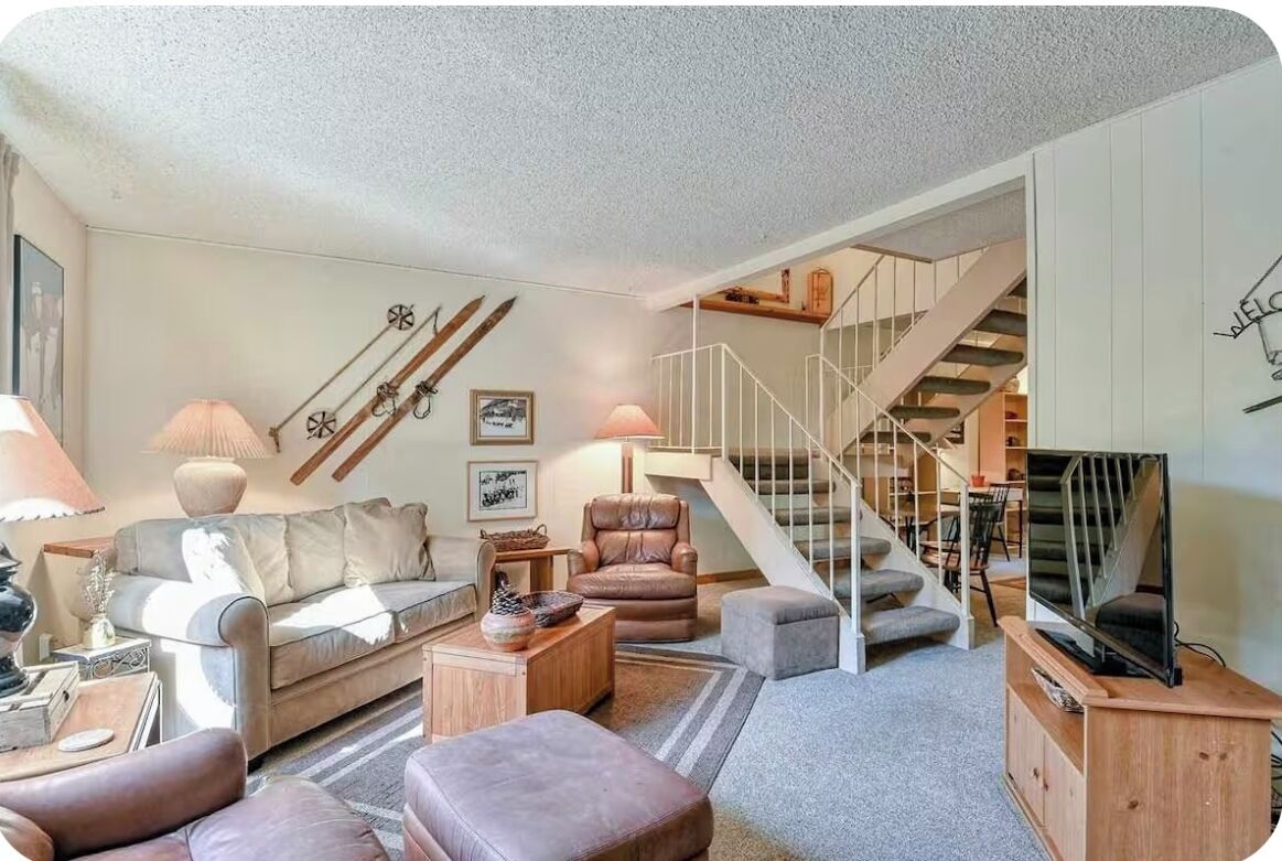 A living room with a sofa, armchairs, a coffee table, a TV stand, and a staircase.