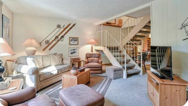 Ein Wohnzimmer mit einer Couch, Sesseln, einem Couchtisch, einem Fernsehtisch und einer Treppe.