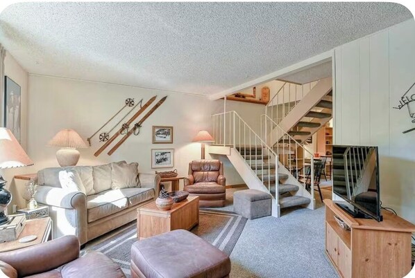 Un salon comprenant un canapé, des fauteuils, une table basse, un meuble pour la télévision et un escalier.