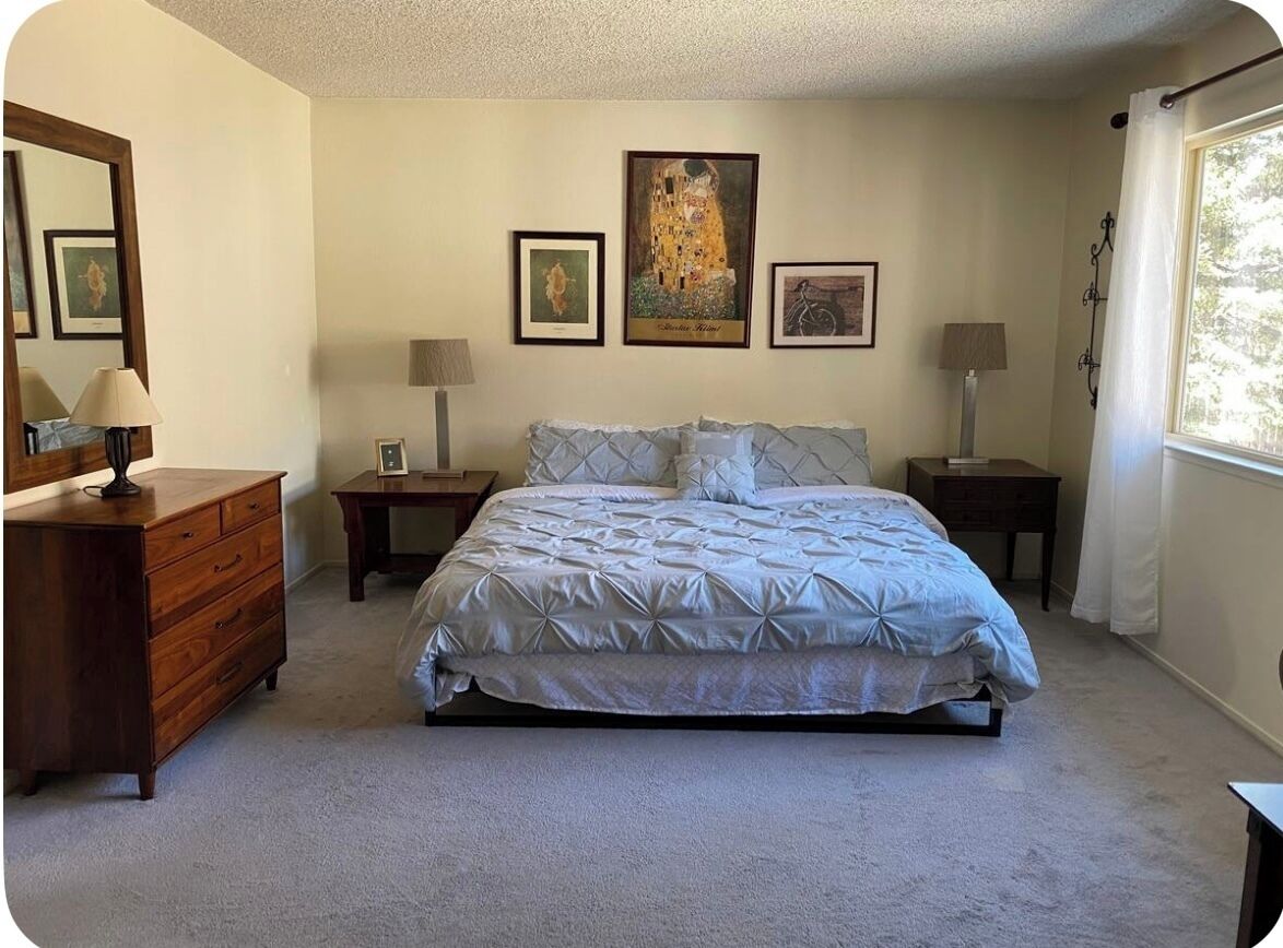 A bedroom with a bed, dresser, nightstands, lamps, and framed artwork on the wall.