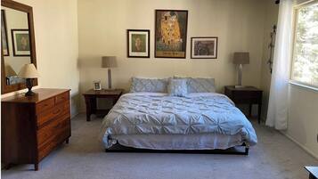 A bedroom with a bed, dresser, nightstands, lamps, and framed artwork on the wall.
