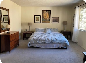 A bedroom with a bed, dresser, nightstands, lamps, and framed artwork on the wall.