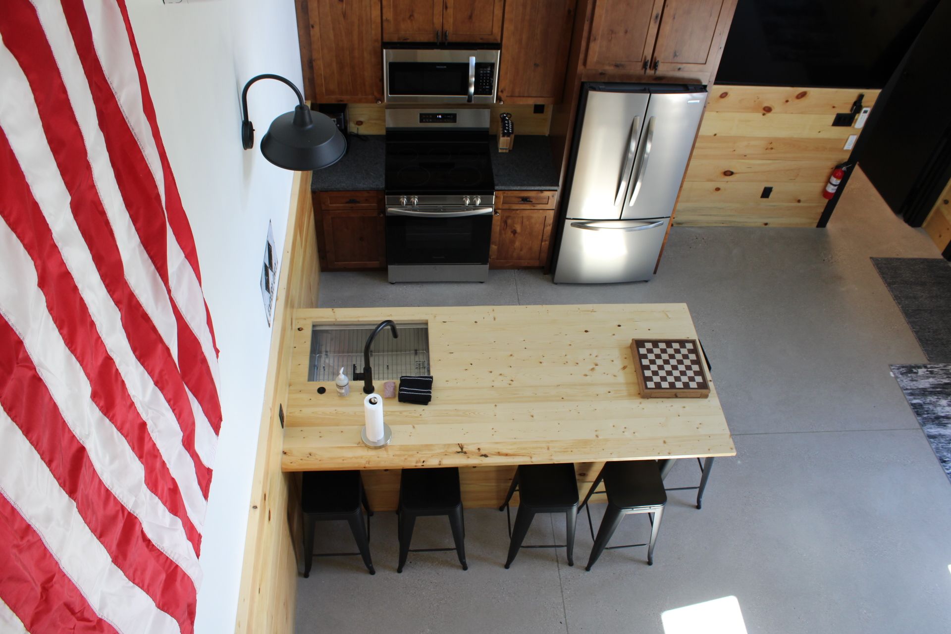 A compact kitchen with wooden cabinets, stainless steel appliances, a wooden table, and four black chairs.