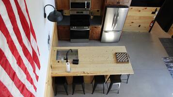 A compact kitchen with wooden cabinets, stainless steel appliances, a wooden table, and four black chairs.