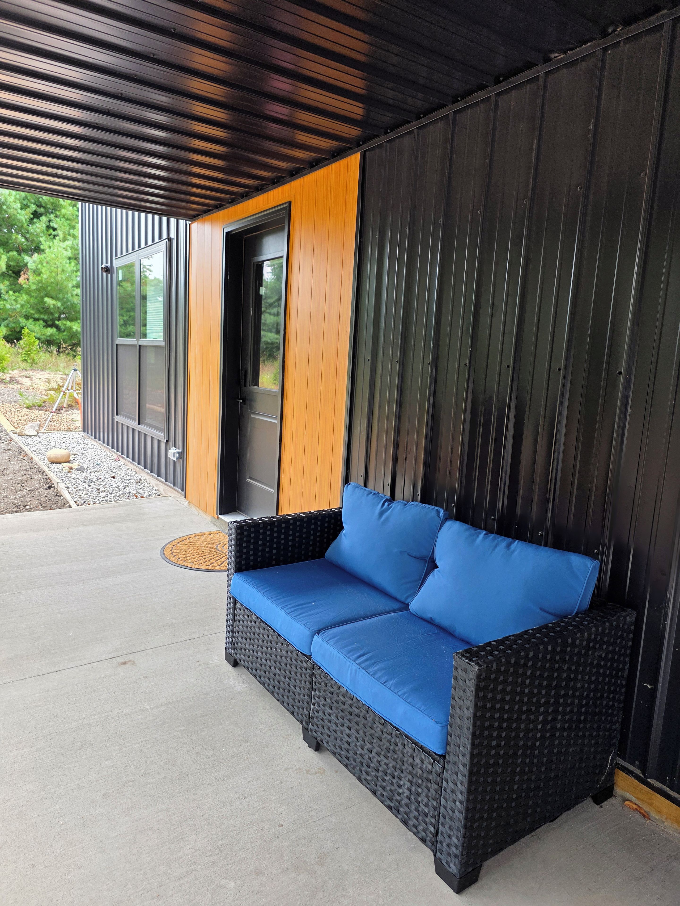 A covered outdoor seating area with a black wicker sofa and blue cushions.