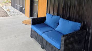 A covered outdoor seating area with a black wicker sofa and blue cushions.