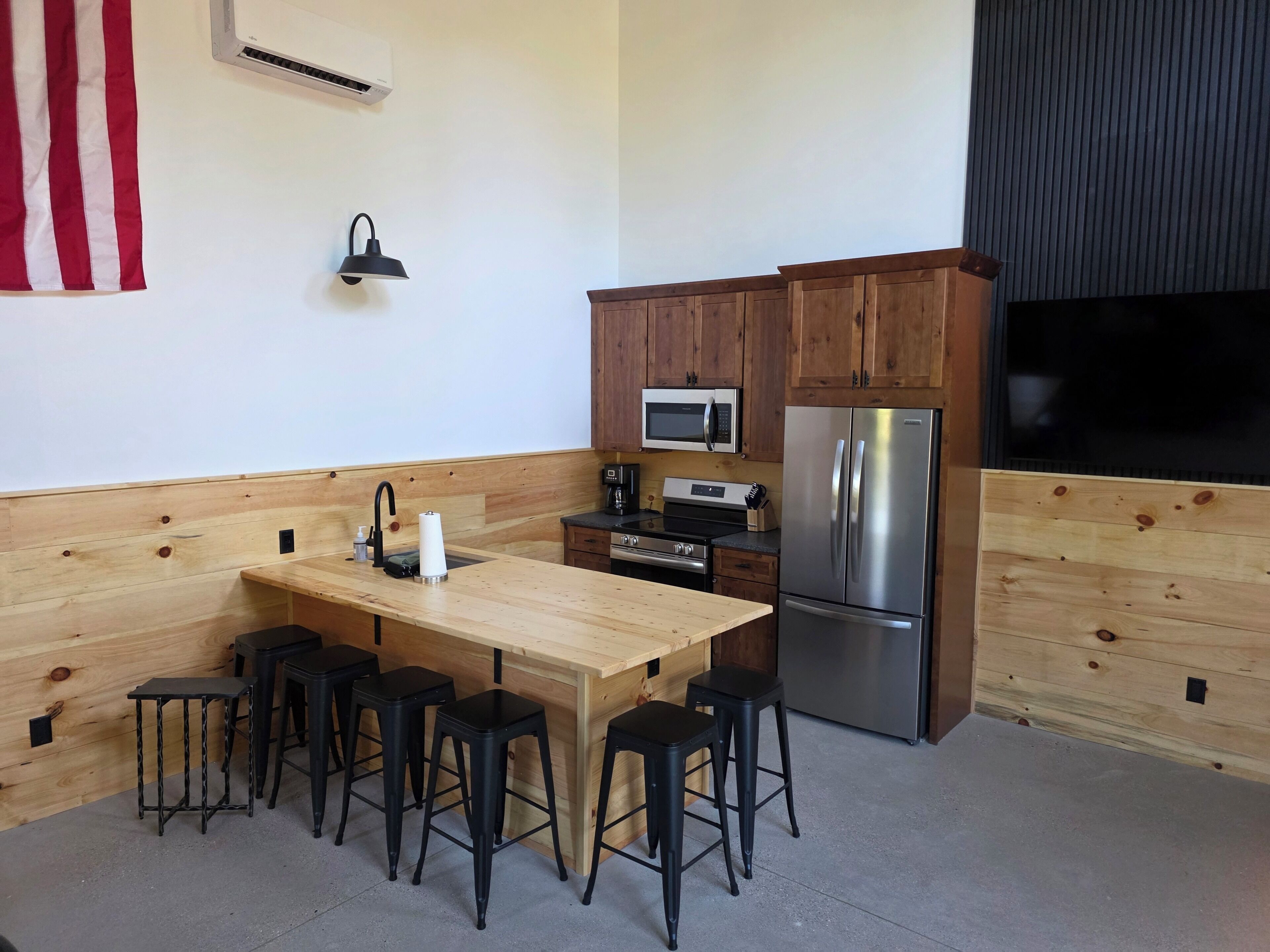 Cozinha com bancada de madeira, eletrodomésticos de aço inoxidável e banquetas pretas.