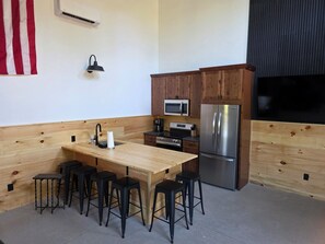 Cozinha com bancada de madeira, eletrodomésticos de aço inoxidável e banquetas pretas.
