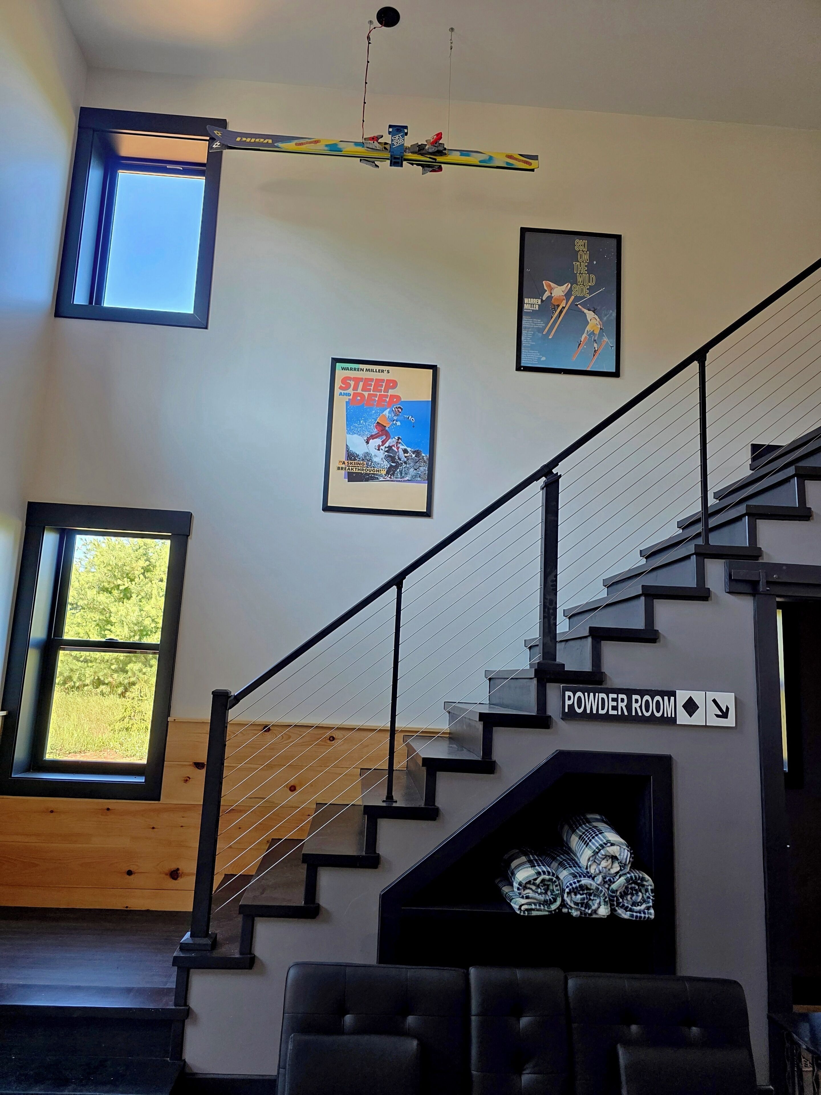 En trappe med et skilt der viser til toiletterne, en indrammet plakat med en snowboarder, og et vindue med udsigt til træer.