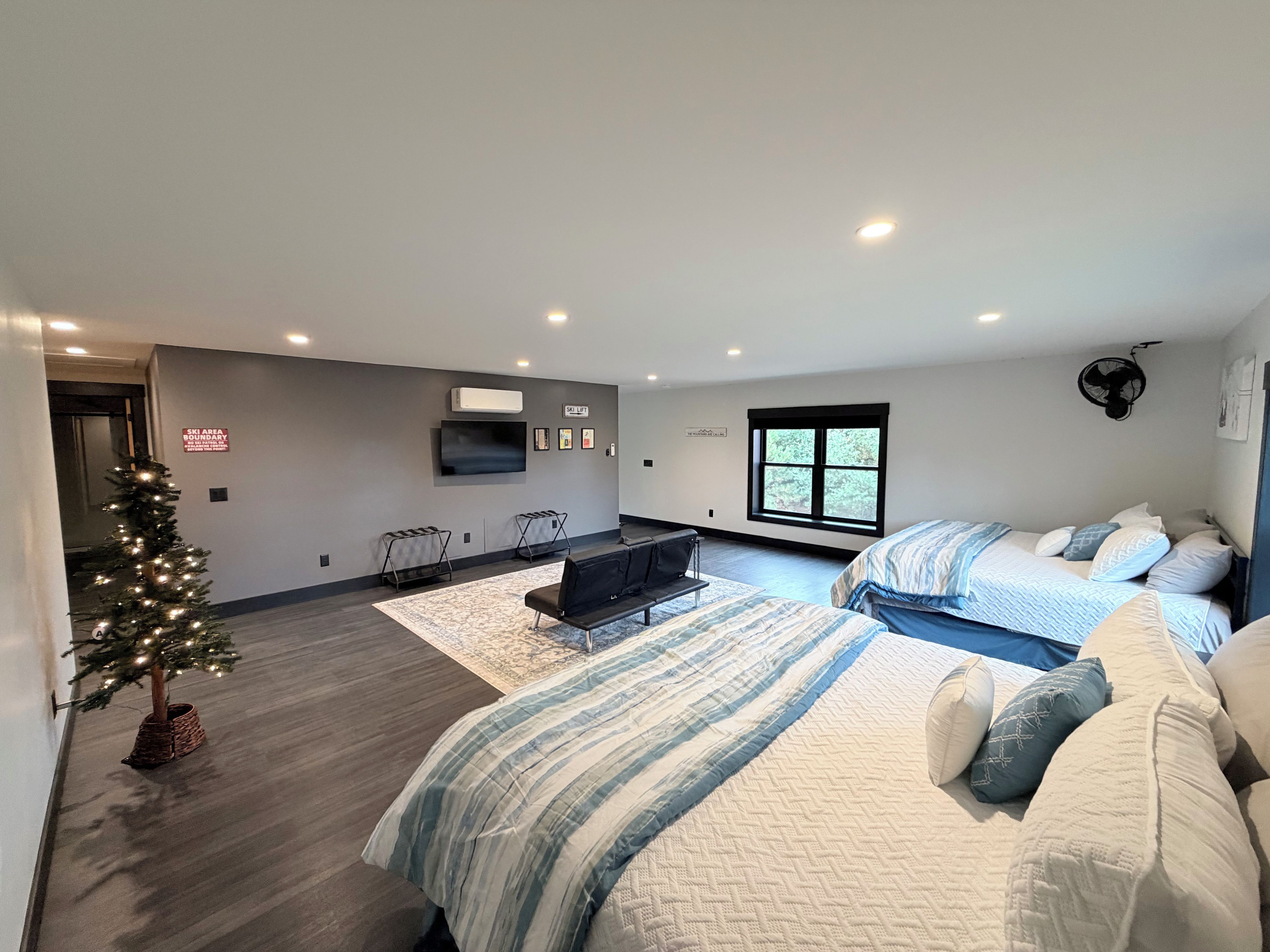 Een moderne hotelkamer met een groot bed, een kleiner bed, een televisie, een kerstboom en een bord met informatie over een skigebied.