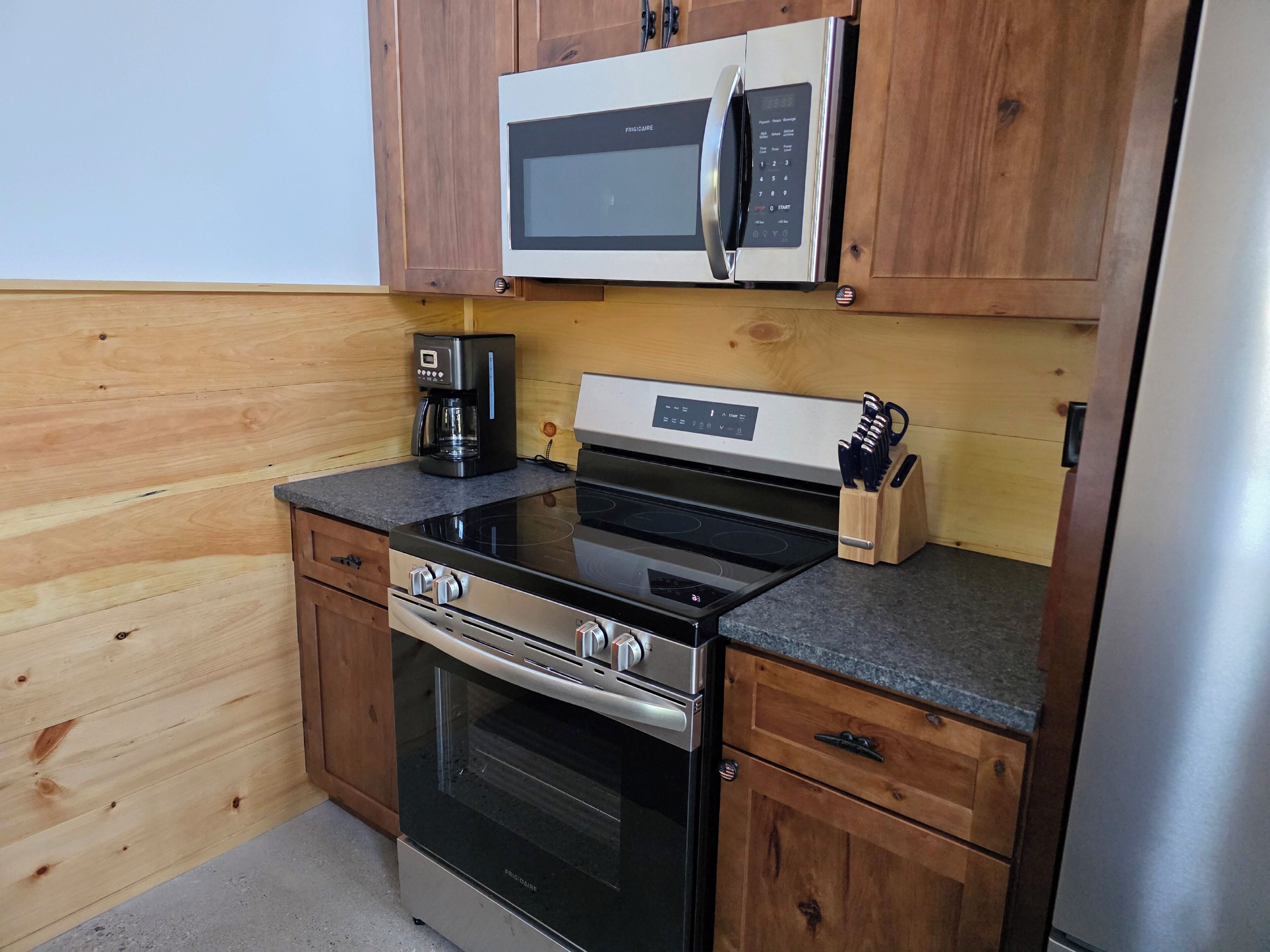 Een praktische keuken met een magnetron, koffiezetapparaat, fornuis, oven en houten keukenkastjes.