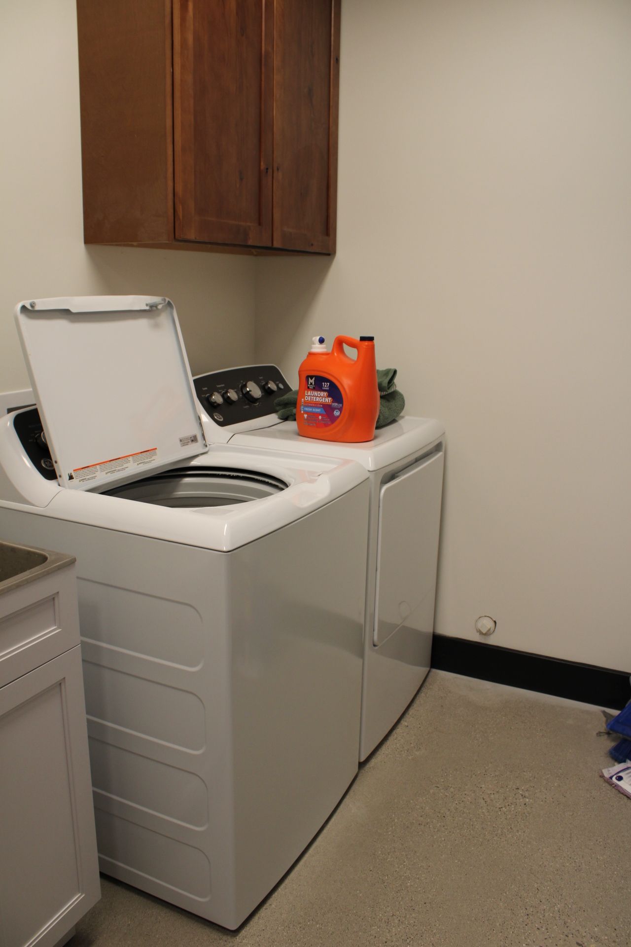 A front-loading washing machine with a detergent bottle on top, a white cabinet, and a wooden cabinet above.