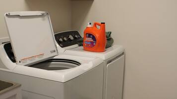 A front-loading washing machine with a detergent bottle on top, a white cabinet, and a wooden cabinet above.