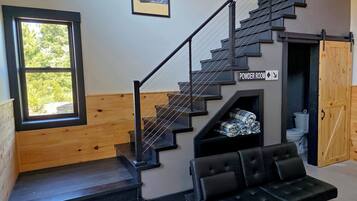 Eine Treppe mit Hinweis auf eine Toilette, ein schwarzes Sofa und ein Fenster mit Blick auf Grünflächen.