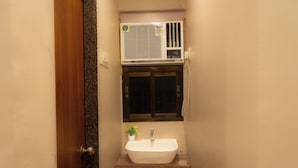 A bathroom with a white sink, a small potted plant, and a window above the mirror.