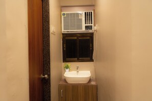 A bathroom with a white sink, a small potted plant, and a window above the mirror. - Hotel Meriton Star  (Ulhasnagar)