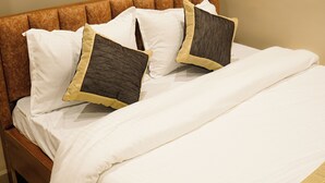 A bed with a wooden headboard, white bedding, and two pillows with a quilted pattern and a gold trim.