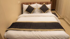A neatly made bed with a dark quilted bedspread and a gold trim, accompanied by white pillows and two dark pillows with gold trim.