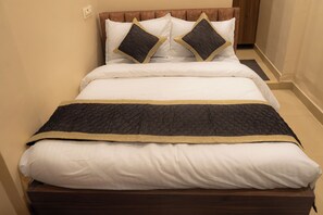 A neatly made bed with a dark quilted bedspread and a gold trim, accompanied by white pillows and two dark pillows with gold trim. - Hotel Meriton Star  (Ulhasnagar)