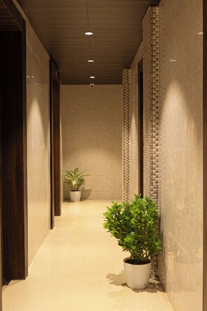 Un couloir avec un sol carrelé, une porte en bois sur la gauche et une plante en pot sur la droite.