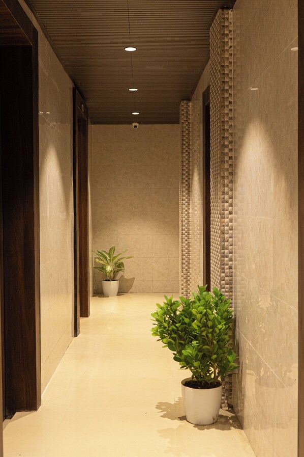 A hallway with a tiled floor, a wooden door on the left, and a potted plant on the right.