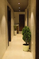 A hallway with a potted tree, a sink, and a door at the end.