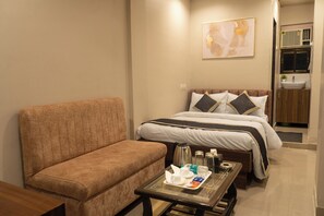 A hotel room with a sofa, a bed with pillows, a bedside table with toiletries, and a painting on the wall.