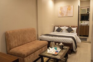 A hotel room with a sofa, a bed with pillows, a bedside table with toiletries, and a painting on the wall.
