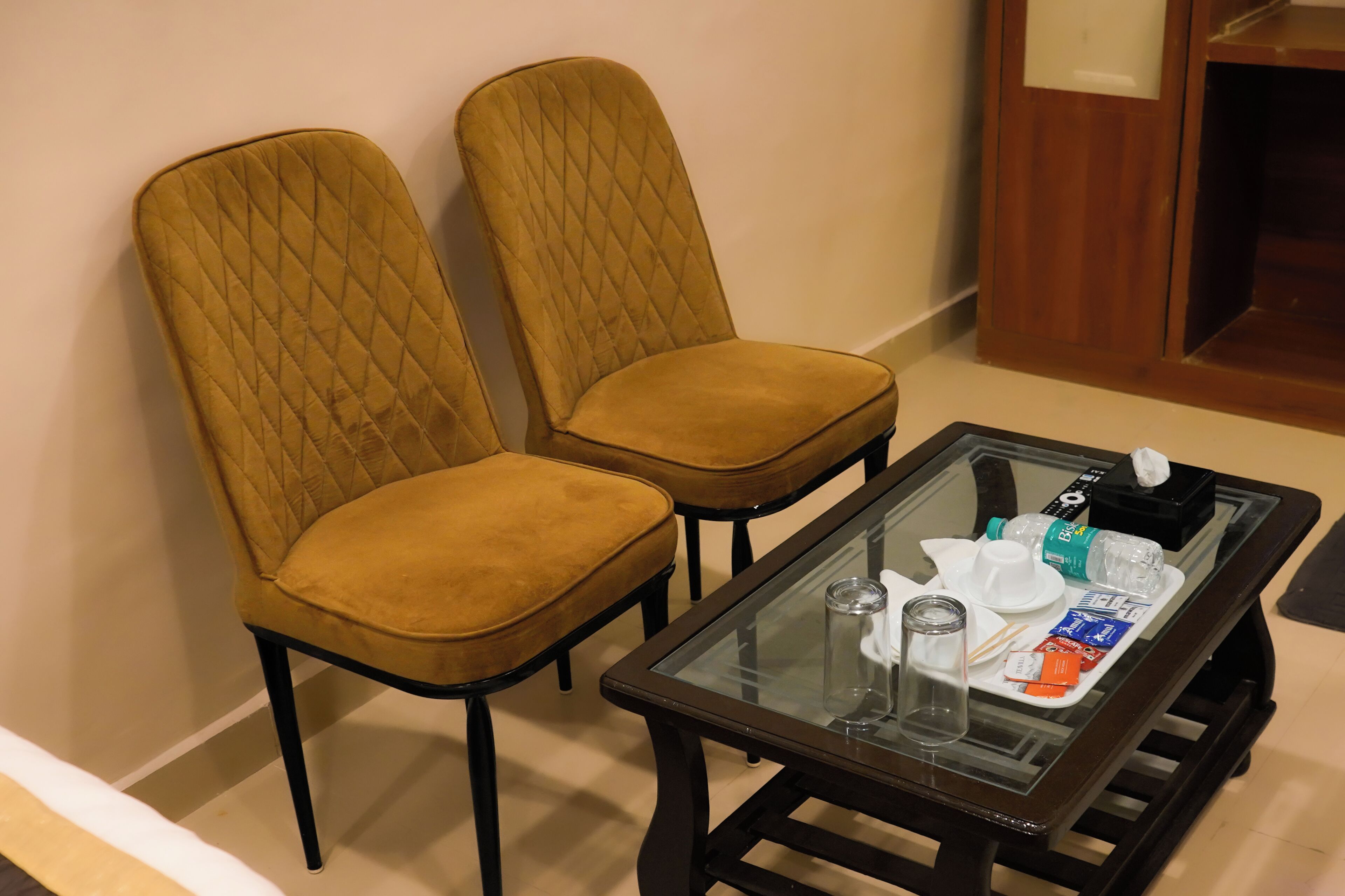 A room with two upholstered chairs and a glass-top table with various items on it.