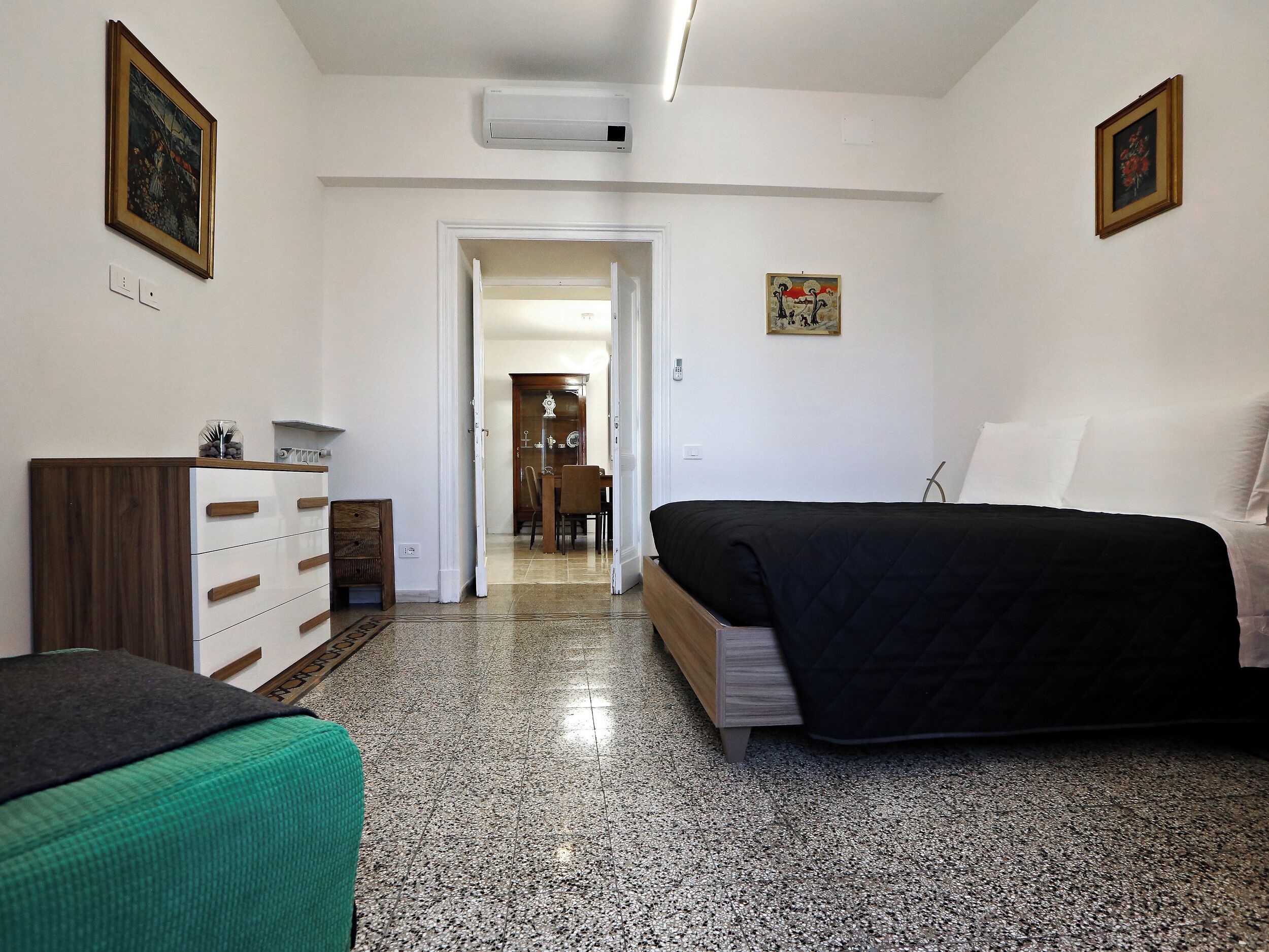 A bedroom with a bed, a dresser, a chair, and a door leading to a bathroom.