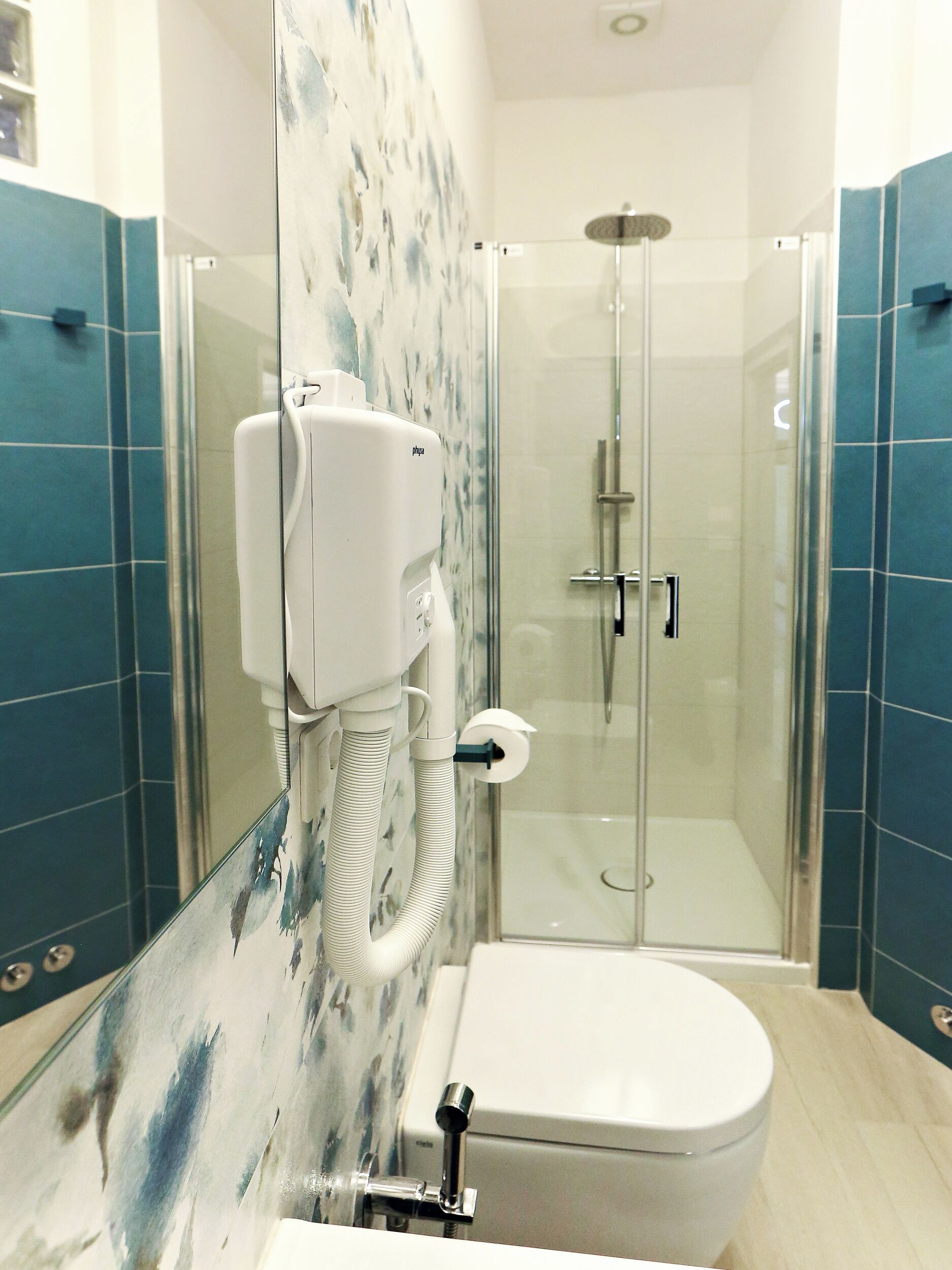 A bathroom with a glass-enclosed shower, a toilet, and a hand dryer mounted on the wall.