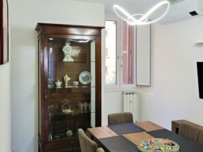 A dining area with a wooden cabinet displaying china, a table with a placemat, and a modern light fixture. - Vanella Luxury Apartment Rome (Roma)