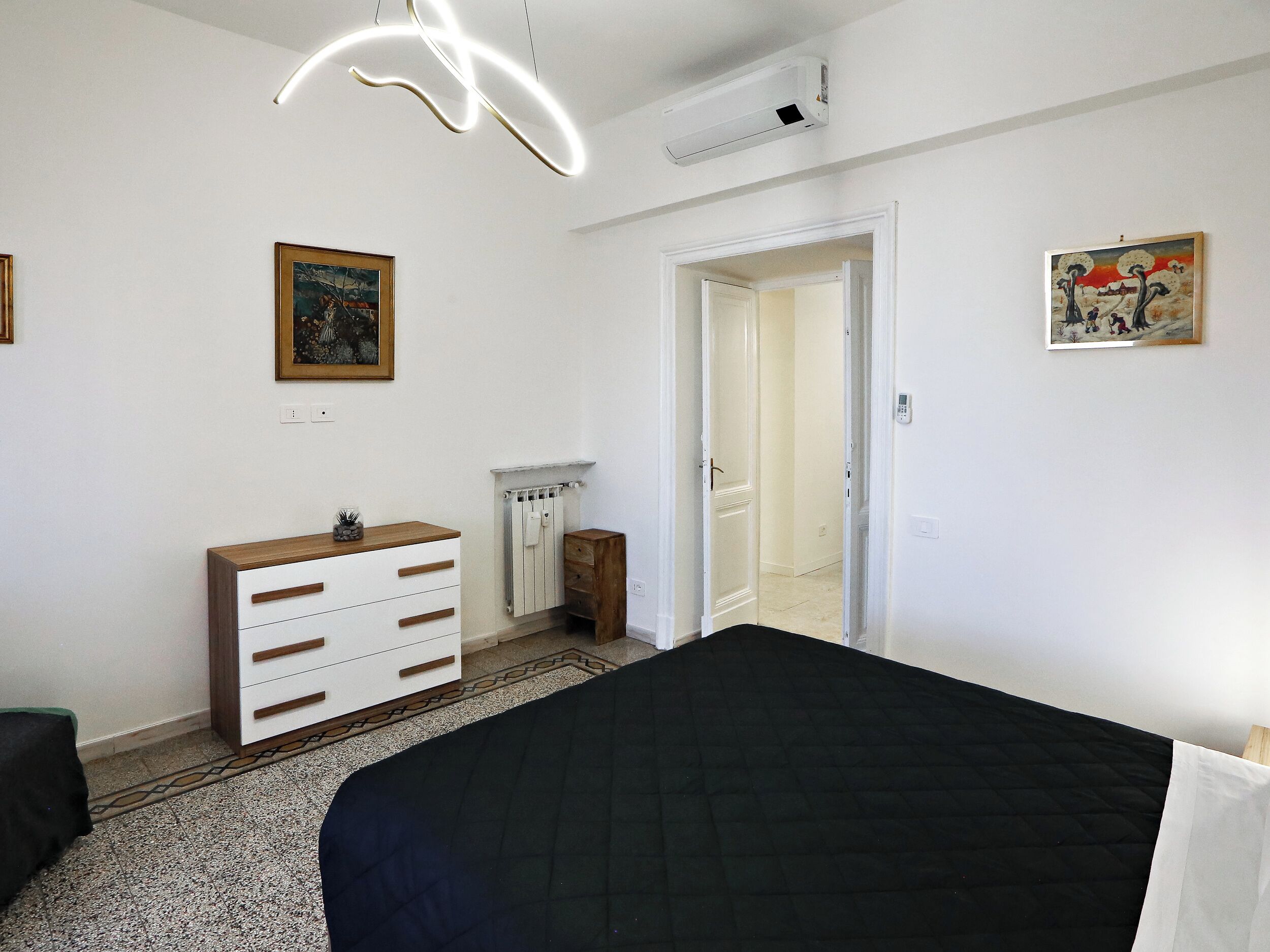 Un dormitorio con cama, cómoda, radiador y dos cuadros en la pared.