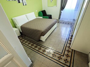 A bedroom with a bed, a nightstand, a green chair, and a patterned floor. - Vanella Luxury Apartment Rome (Roma)