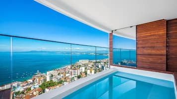 Un balcón moderno con barandilla de cristal que ofrece vistas a la ciudad y al mar.