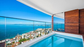 Un balcón moderno con barandilla de cristal que ofrece vistas a la ciudad y al mar.
