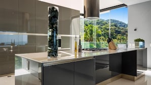 Una cuina moderna amb una illa gran, electrodomèstics d'acer inoxidable i vista a un paisatge exuberat.