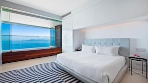 Un dormitori modern amb un llit gran, vistes a l'oceà i una paret de vidre.