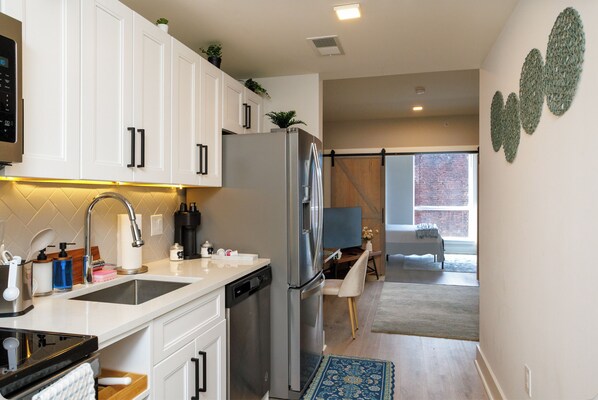 A modern kitchen with white cabinetry, stainless steel appliances, and a view into a dining area with a brick wall. - Stylish Fishtown 1BR - Prime Location (Philadelphia)